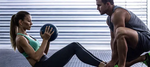 Fitnesstrainer mit Ausbildung hilft Frau beim Training.