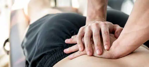 Regenerations- und Sportmasseur - Therapeut, der männlichen Athleten in der Klinik eine niedrigere Rückensportmassage gibt