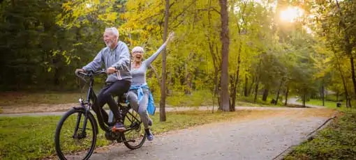 Aktivierung durch Bewegung | Fröhliches aktives Seniorenpaar mit Fahrrad im öffentlichen Park zusammen Spaß zu haben. Perfekte Aktivitäten für ältere Menschen.
