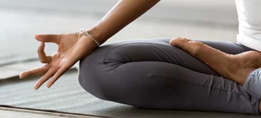 Fernstudium Vinyasa Yoga | Afrikanische Frau, die aktive Kleidung trägt, macht Yoga Meditieren im Haus, Nahaufnahme Foto Lotus Position. 