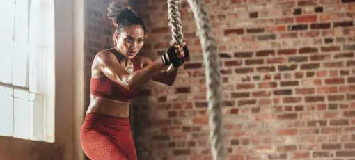 Crosstraining Ausbildung | Fit und muskulöse Frau, die im Fitnessstudio mit Angeln trainiert. Frauensportler, die im Fitnessstudio Schlachtseil trainieren.