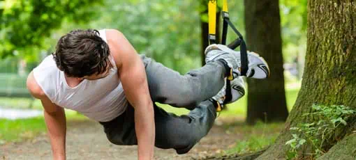 Schlingentrainer Ausbildung  | Junge Sporttrainer trainieren im City Park unter Sommerbäumen für sportliche Fitness