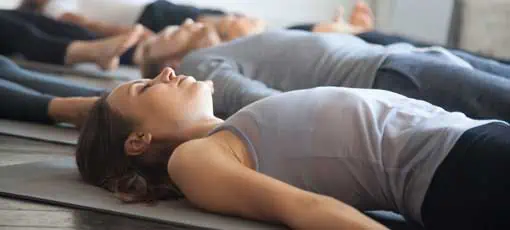 Gruppe junger sportlicher Leute, die Yoga-Unterricht mit Trainer im Fitnessstudio machen, in Dead Body trainieren, Savasana machen, Corpse Pose, Freunde, die sich nach dem Training im Sportclub entspannen, Studiobild